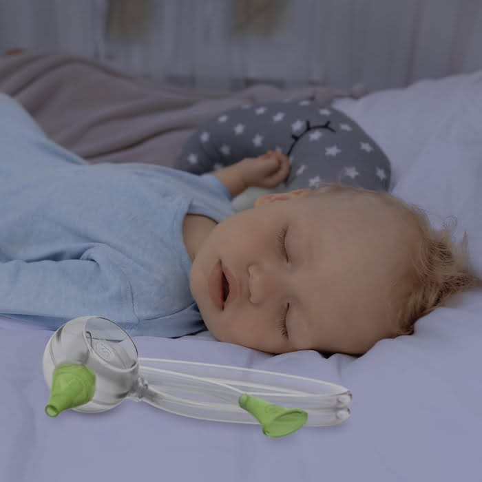 Un bambino dorme tranquillamente nel suo letto accanto all'aspiratore nasale manuale Nosiboo Eco