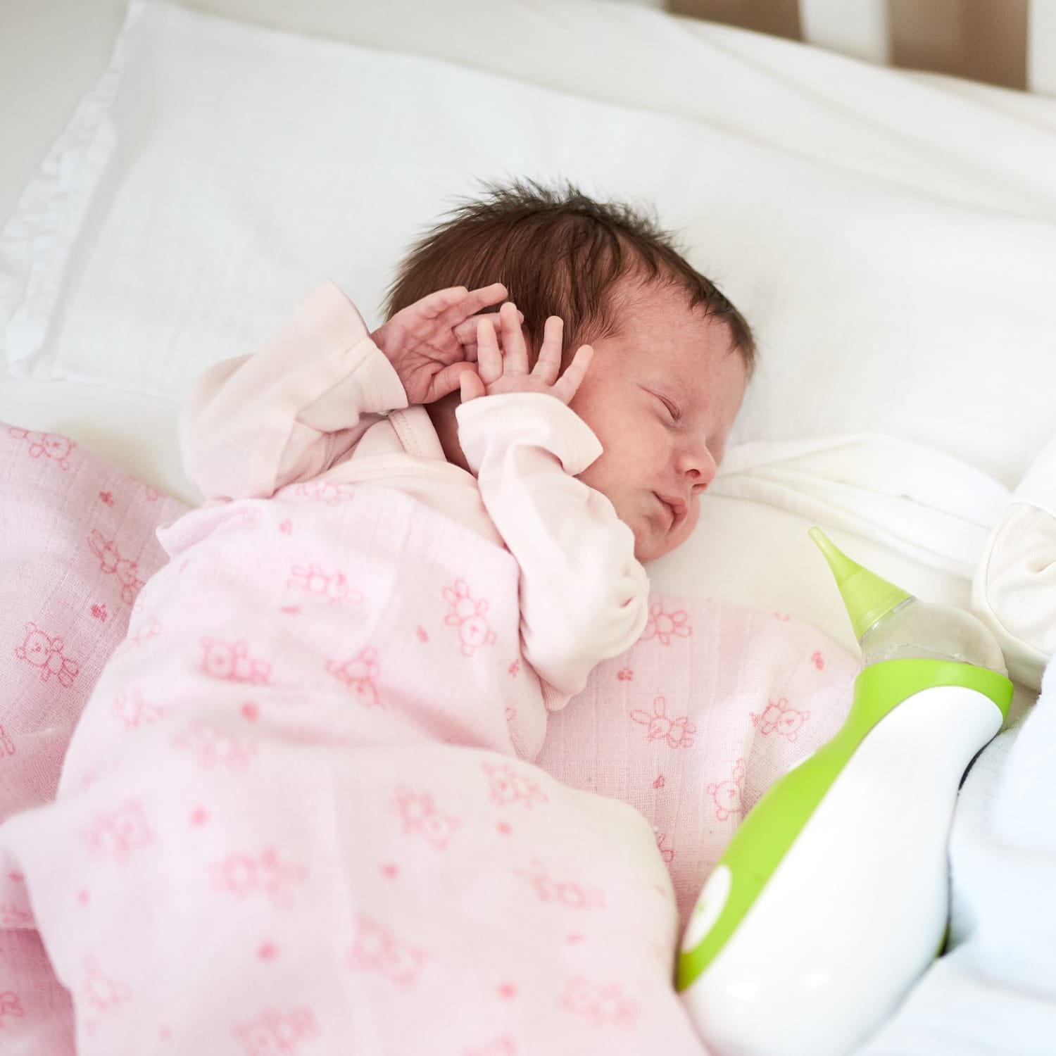 Un neonato che dorme in un letto accanto a un aspiratore nasale portatile Nosiboo Go.